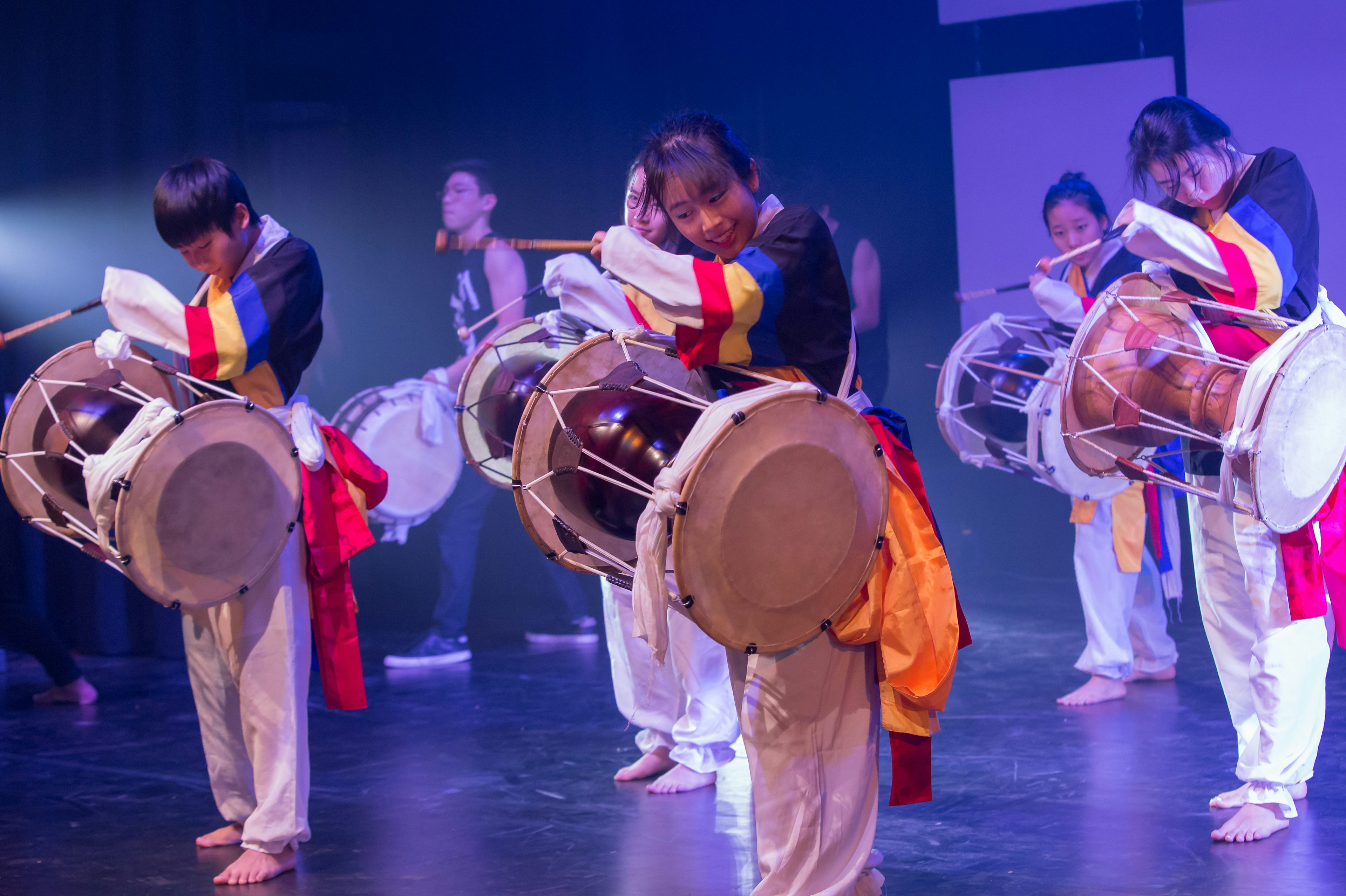 Three students are playing music on large drums