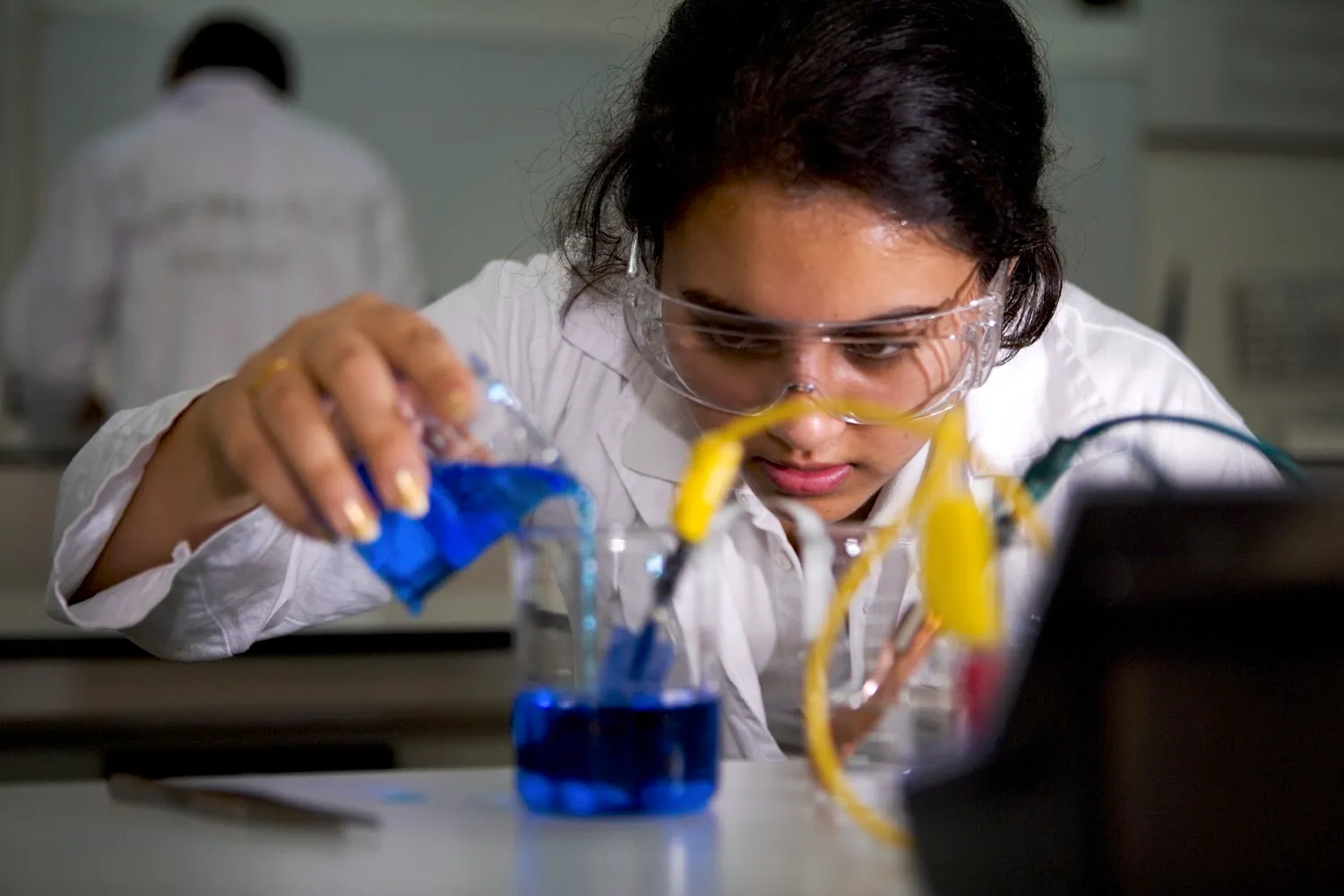 A girl is carefully pouring a blue liquid into a glass as part of a chemistry experiment