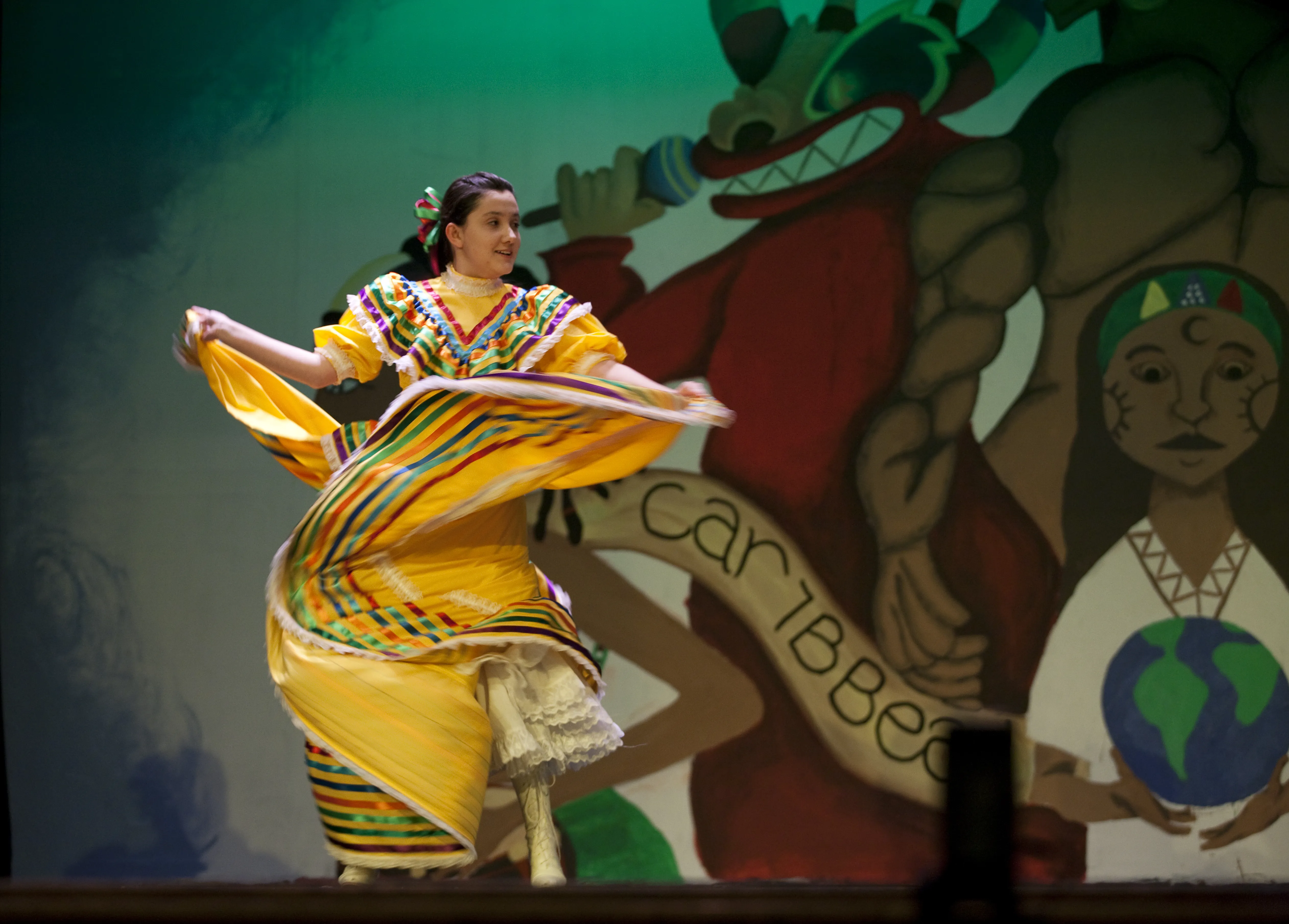 A girl in a wide yellow dress is dancing in front of a mural