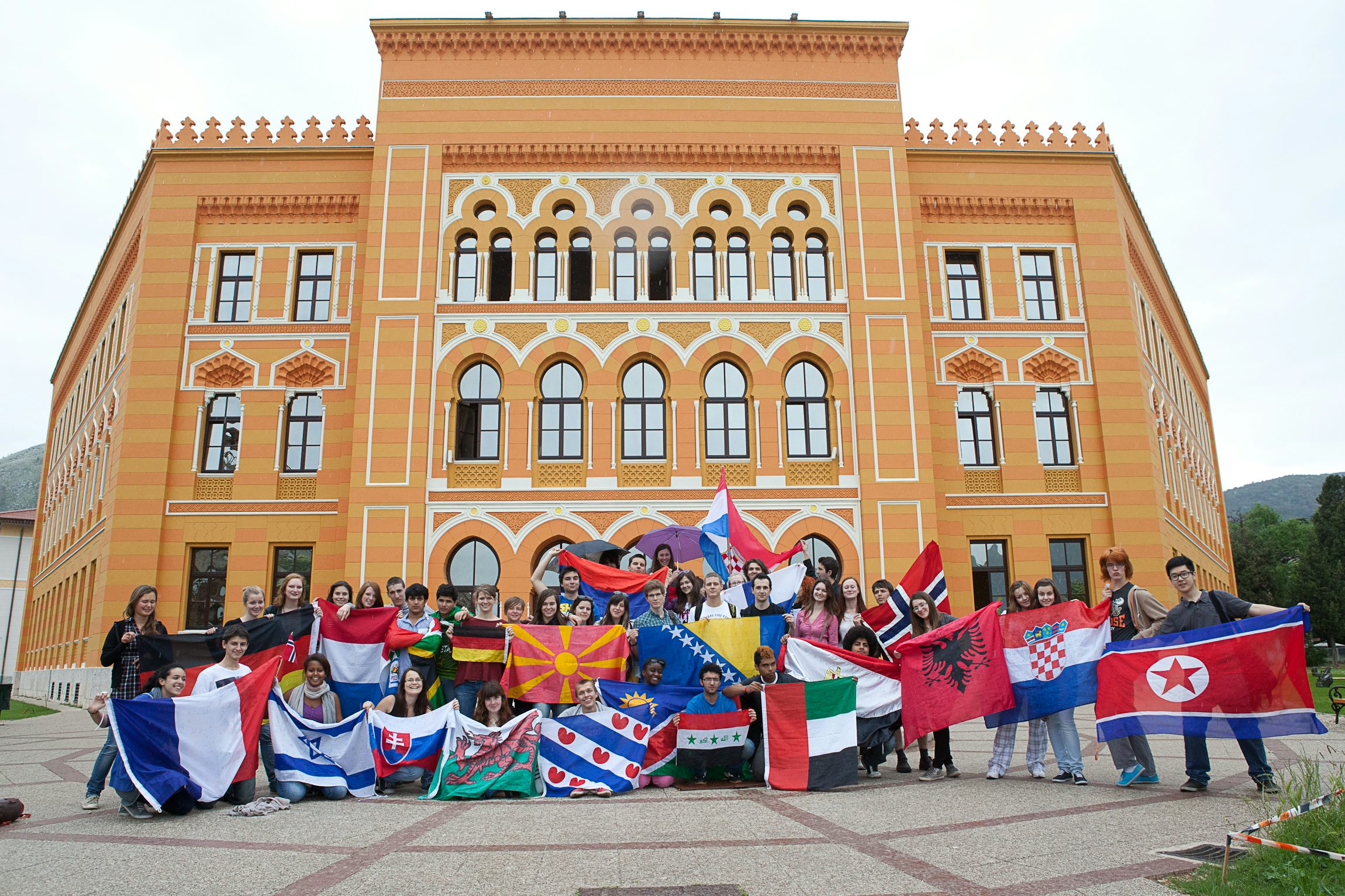 A group of students with flags is posing in front of the UWC school building in Mostar
