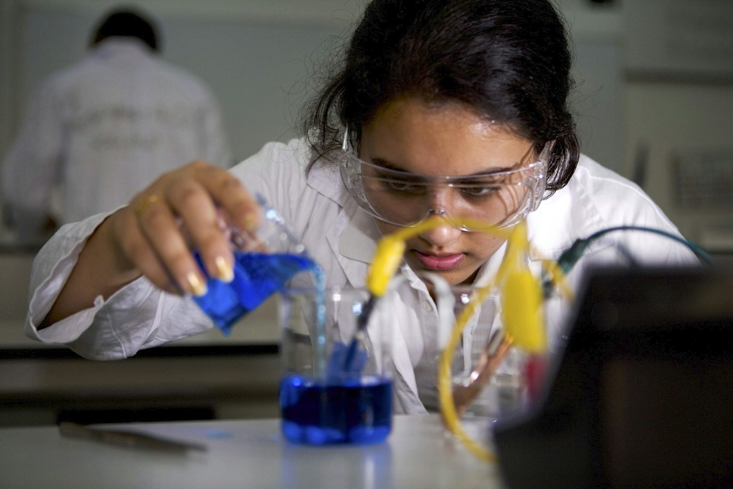 A girl is carefully pouring a blue liquid into a glass as part of a chemistry experiment
