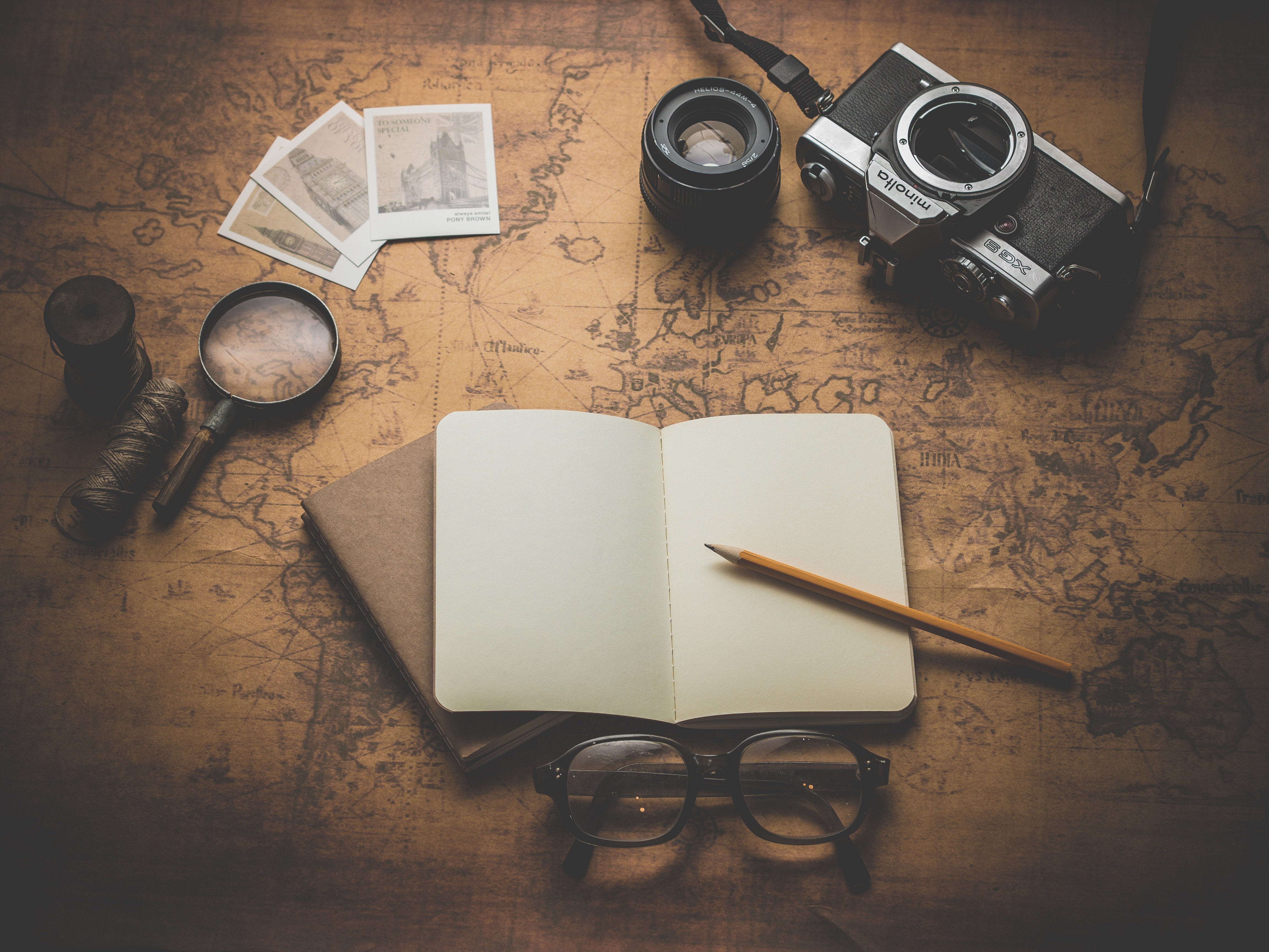 An open and empty journal rests on top of a map next to a camera and a pair of glasses.